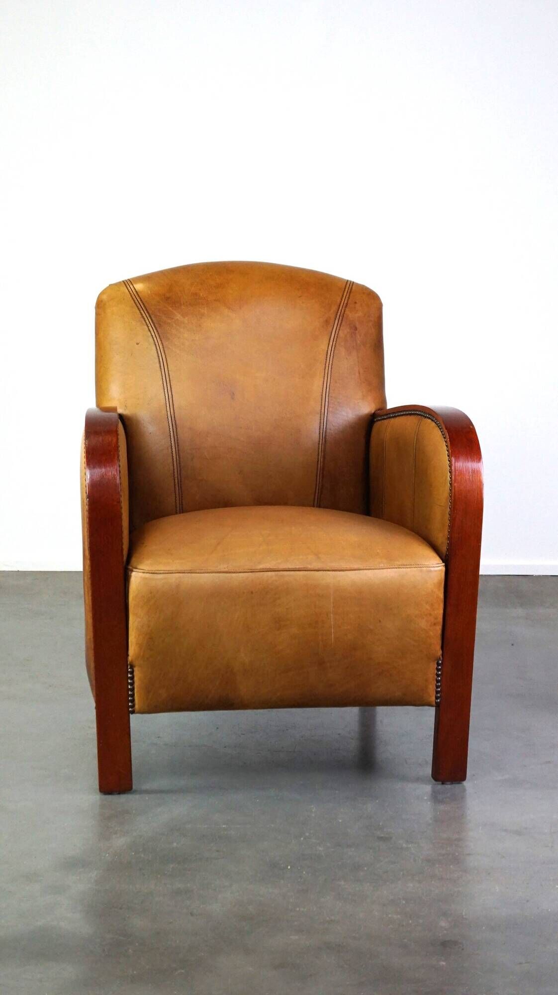Luxurious cowhide Art Deco design armchair with wooden armrests and cognac-colored leather