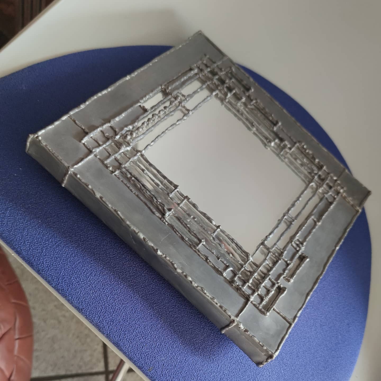 Pewter mirror on a brutalist-style wooden stand