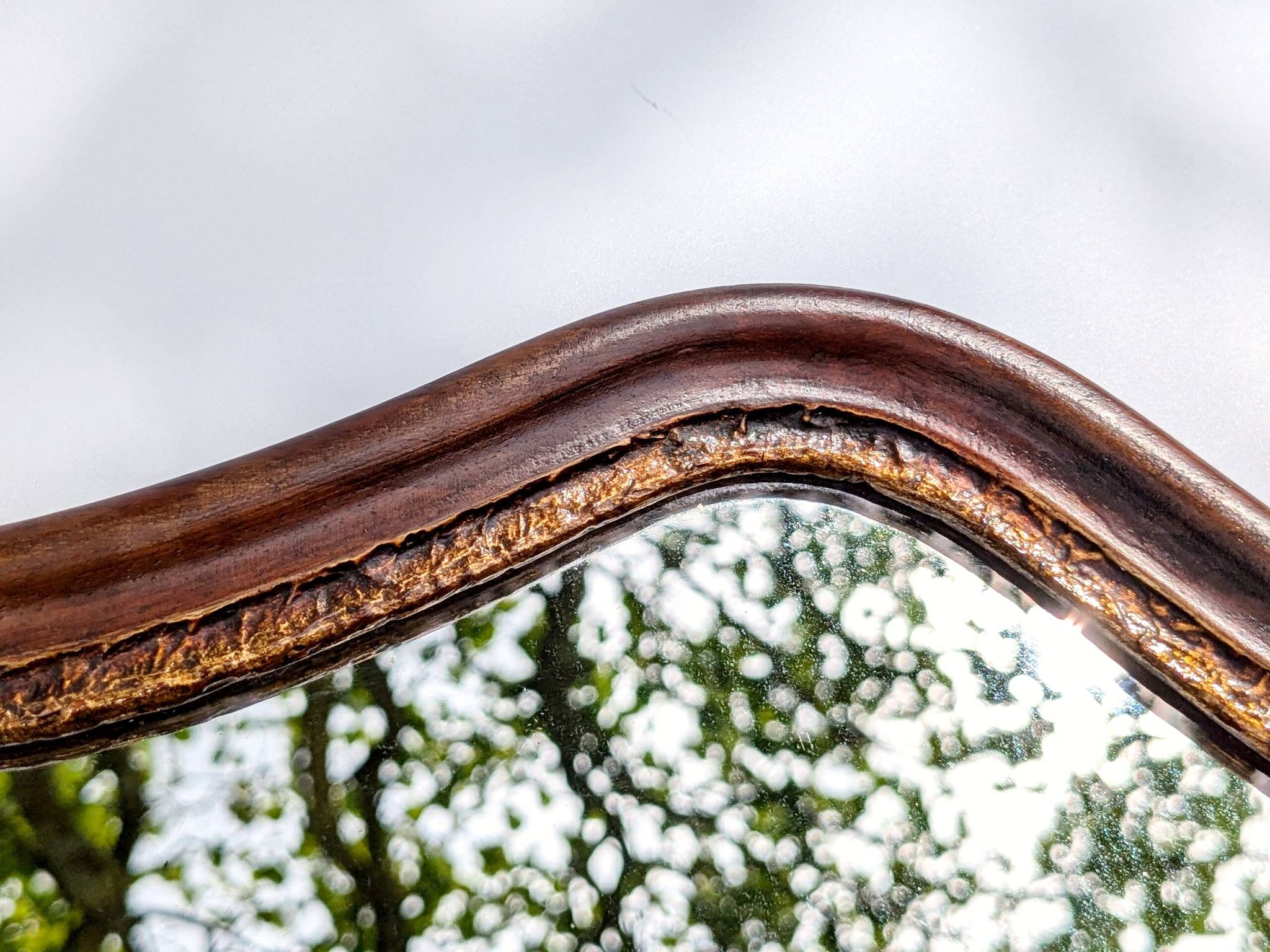 Antique wall mirror in carved wood with a wavy shape and a golden trim.