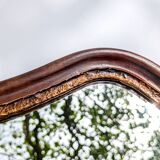 Antique wall mirror in carved wood with a wavy shape and a golden trim.