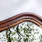 Antique wall mirror in carved wood with a wavy shape and a golden trim.