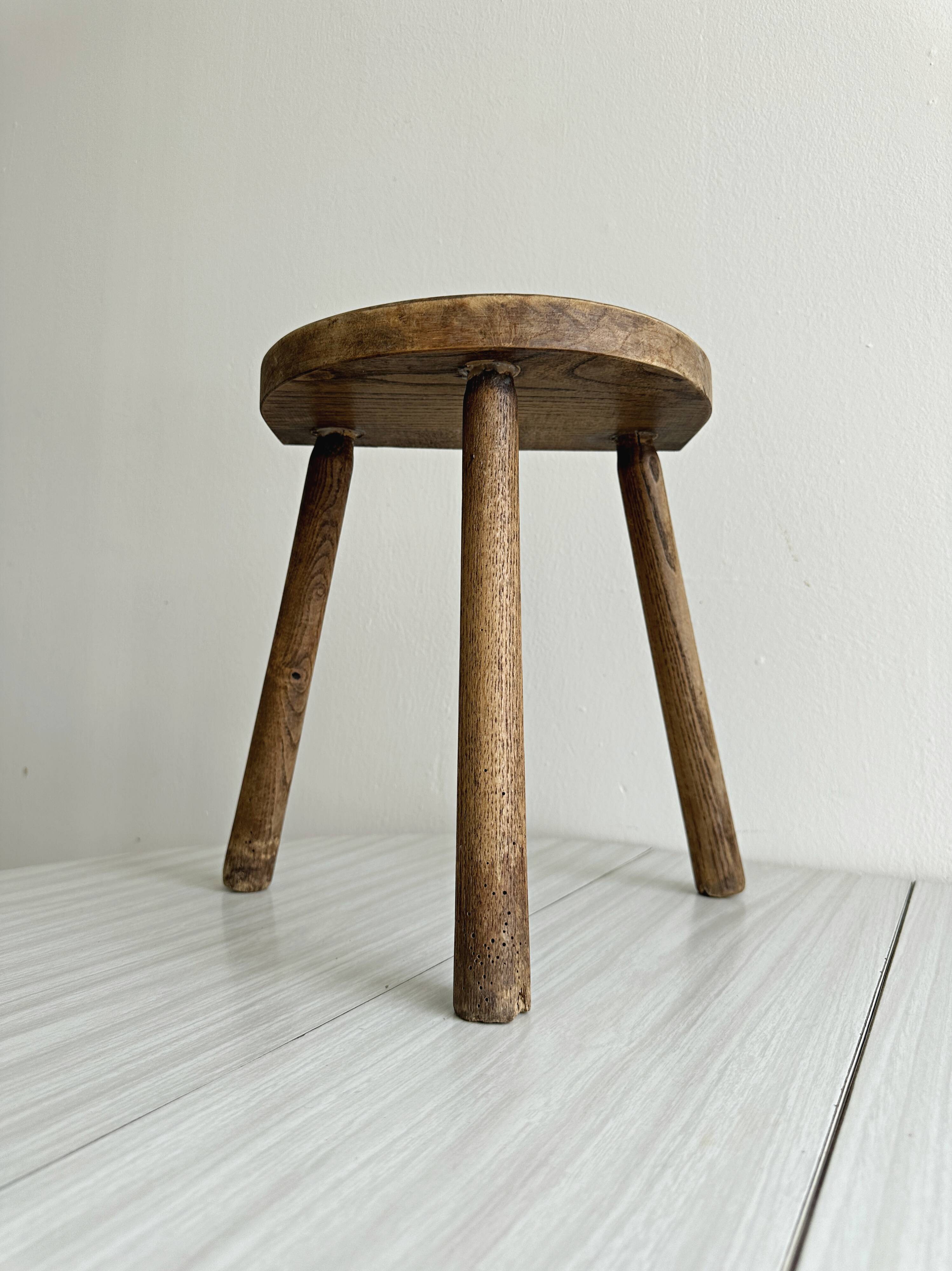 Small antique tripod stool in light wood, half-moon seat.