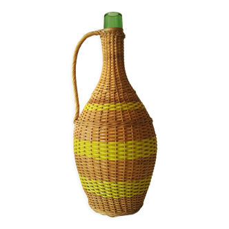 Vintage glass bottle covered with hand-woven wicker and scoubidou, with a handle