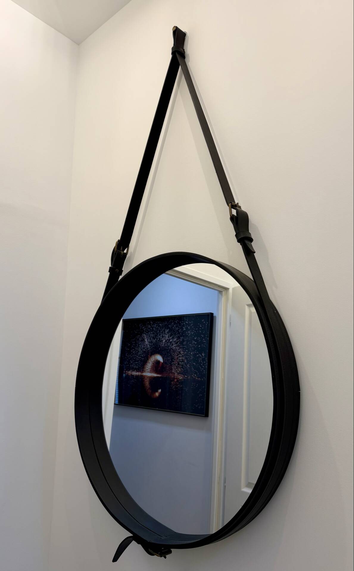 Round mirror covered in black leather in the style of Jacques Adnet.
