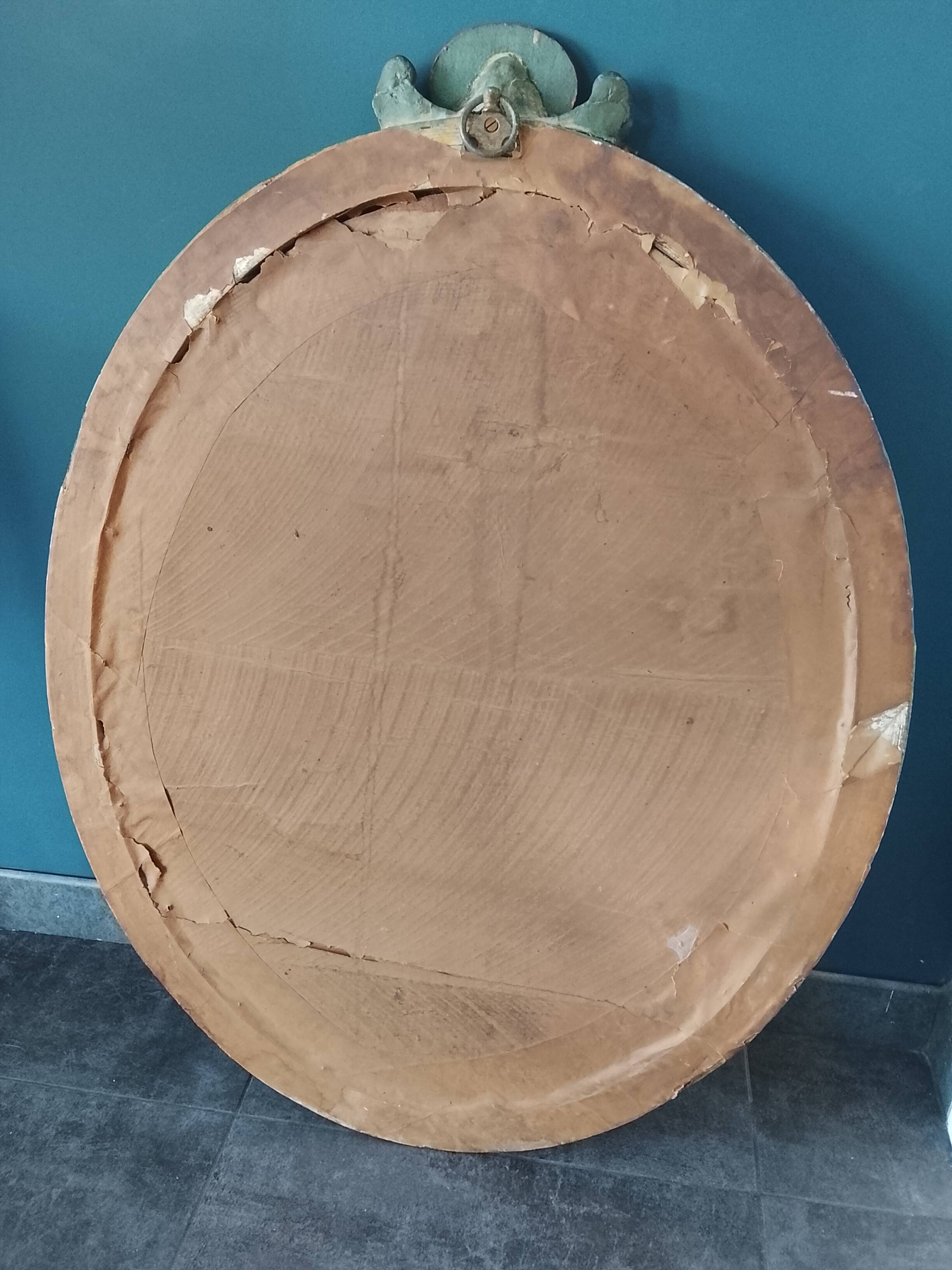 Antique oval mirror in a carved and painted frame with a floral panel.