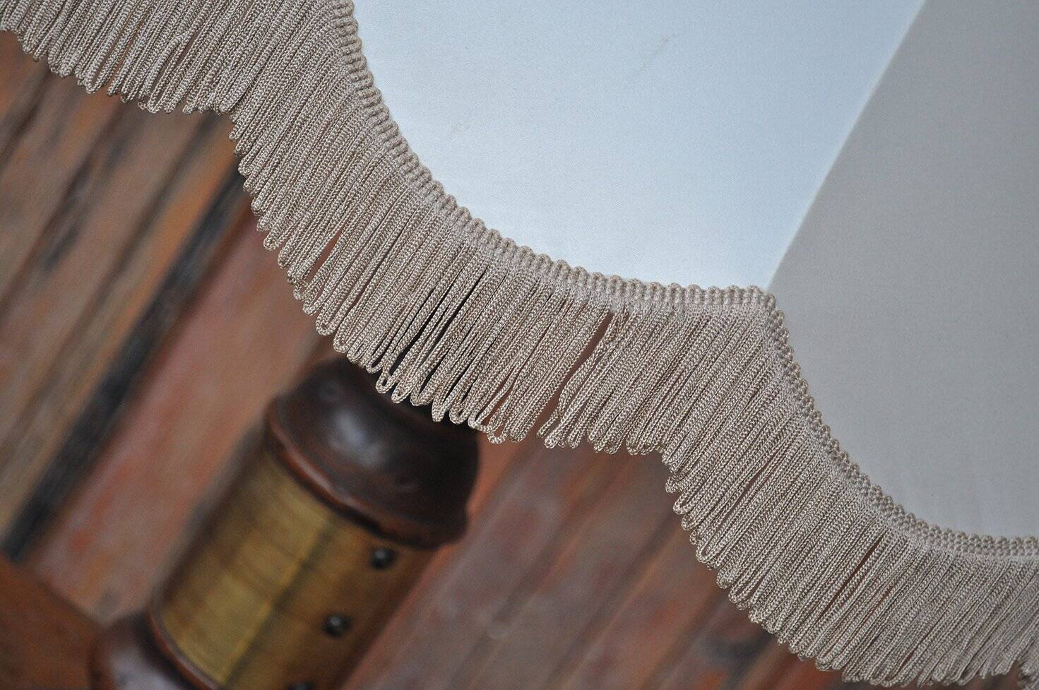 Vintage brown and gold desk lamp made of carved wood and brass, with a fringed shade.