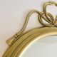 Decorative oval mirror in brass adorned with a large twisted bow.
