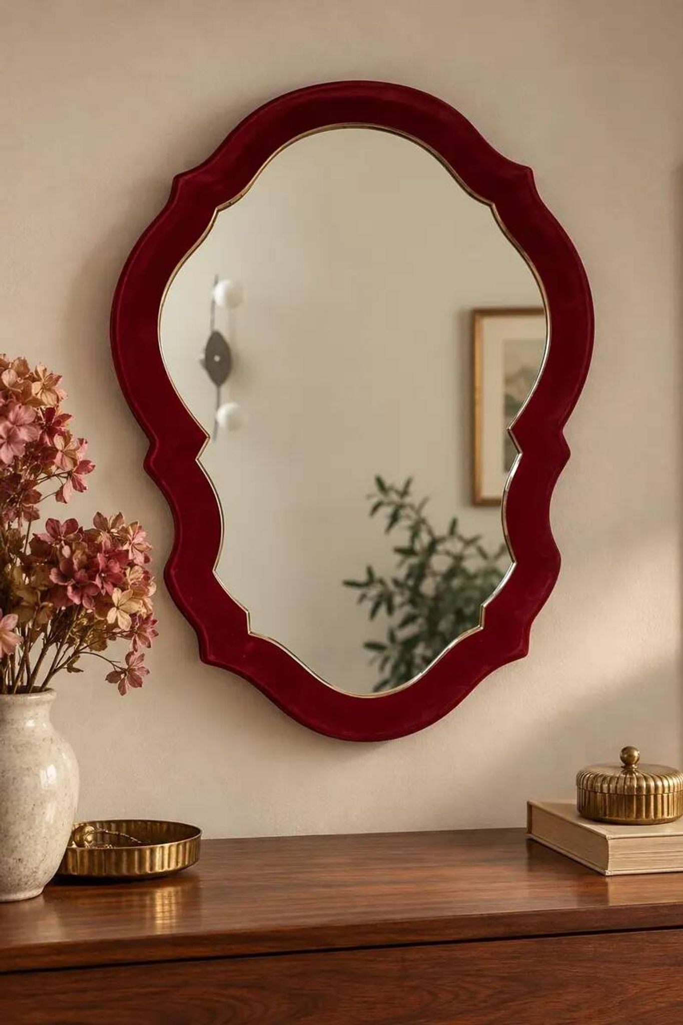 Vintage mirror with a scalloped shape in burgundy velvet and a golden trim.