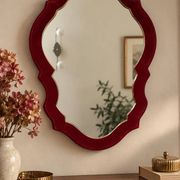 Vintage mirror with a scalloped shape in burgundy velvet and a golden trim.