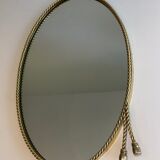 Oval brass mirror surrounded by a cord and adorned