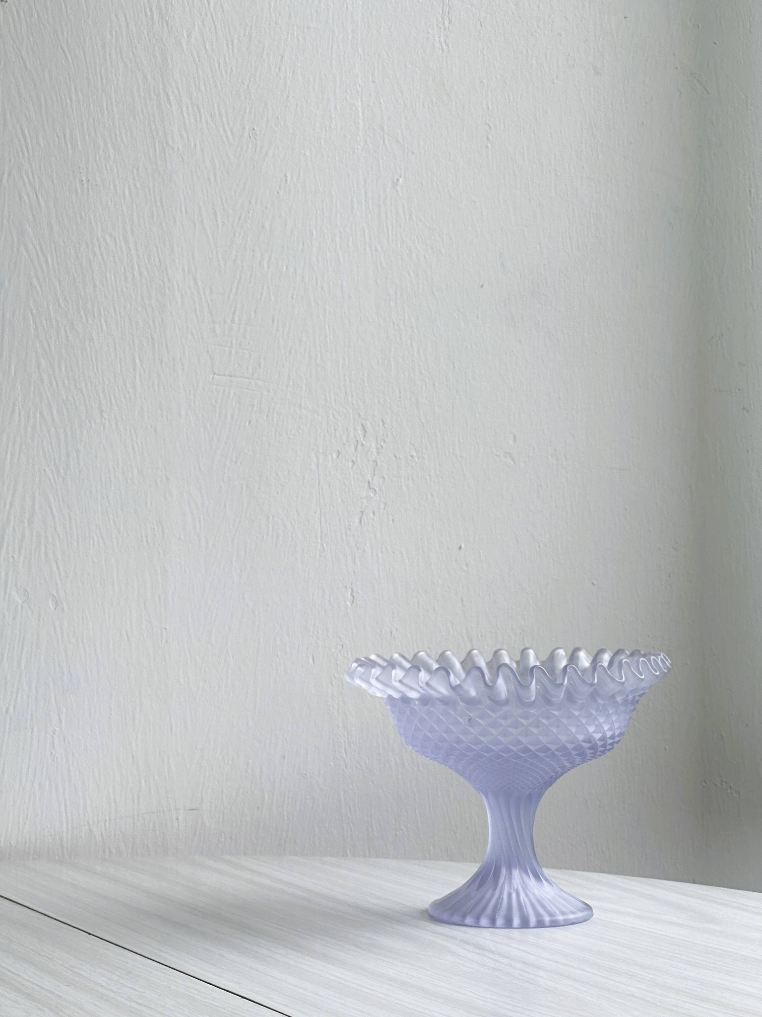 Purple glass pedestal bowl with wavy border and relief pattern.