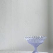 Purple glass pedestal bowl with wavy border and relief pattern.