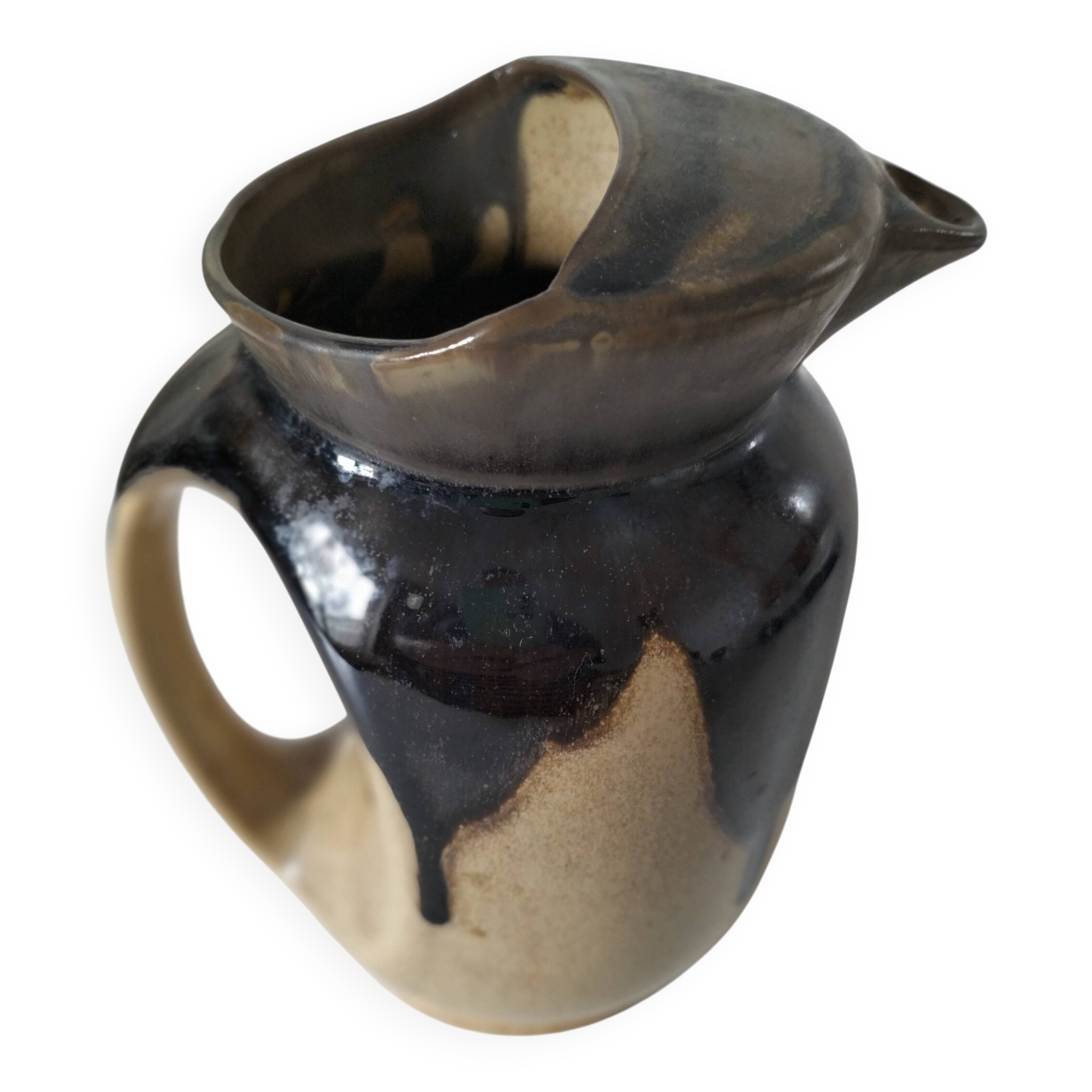 Stoneware jug with deep black drips on a sandy background.