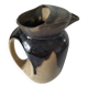 Stoneware jug with deep black drips on a sandy background.