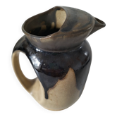 Stoneware jug with deep black drips on a sandy background.