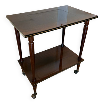 Vintage varnished wooden side table, on wheels with golden trim.