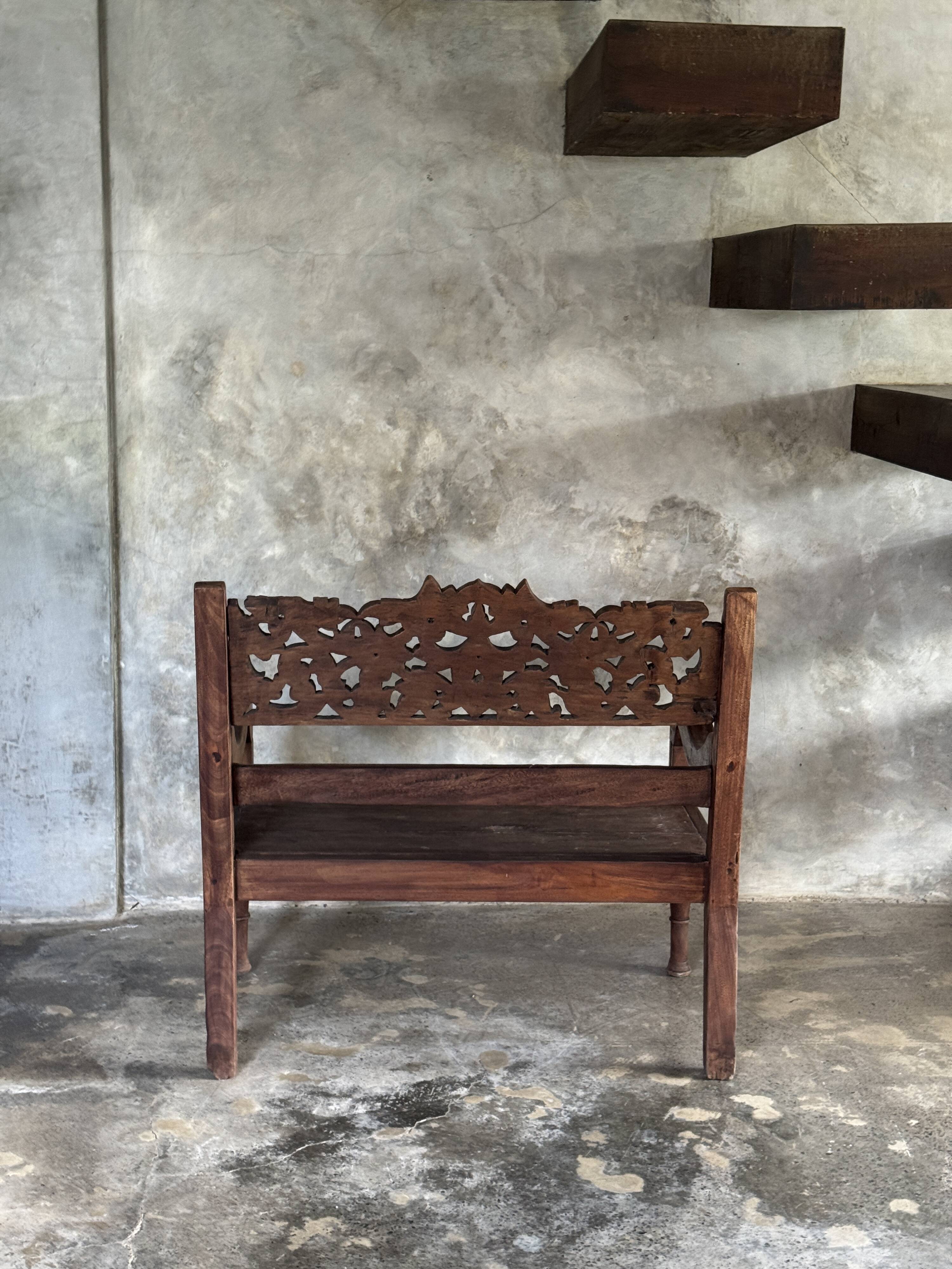 Small antique Indonesian bench in carved teak with plant and floral motifs.