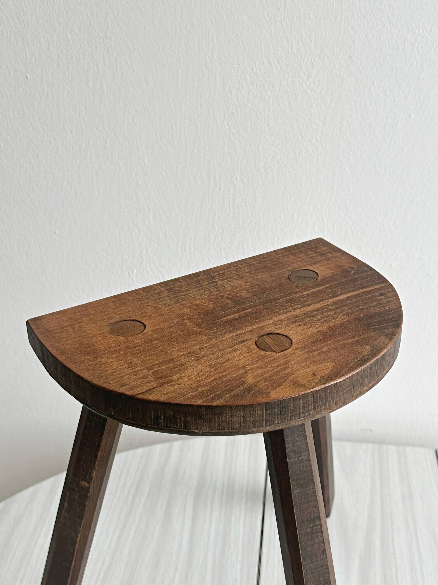 Antique wooden tripod stool with a semi-circular seat.