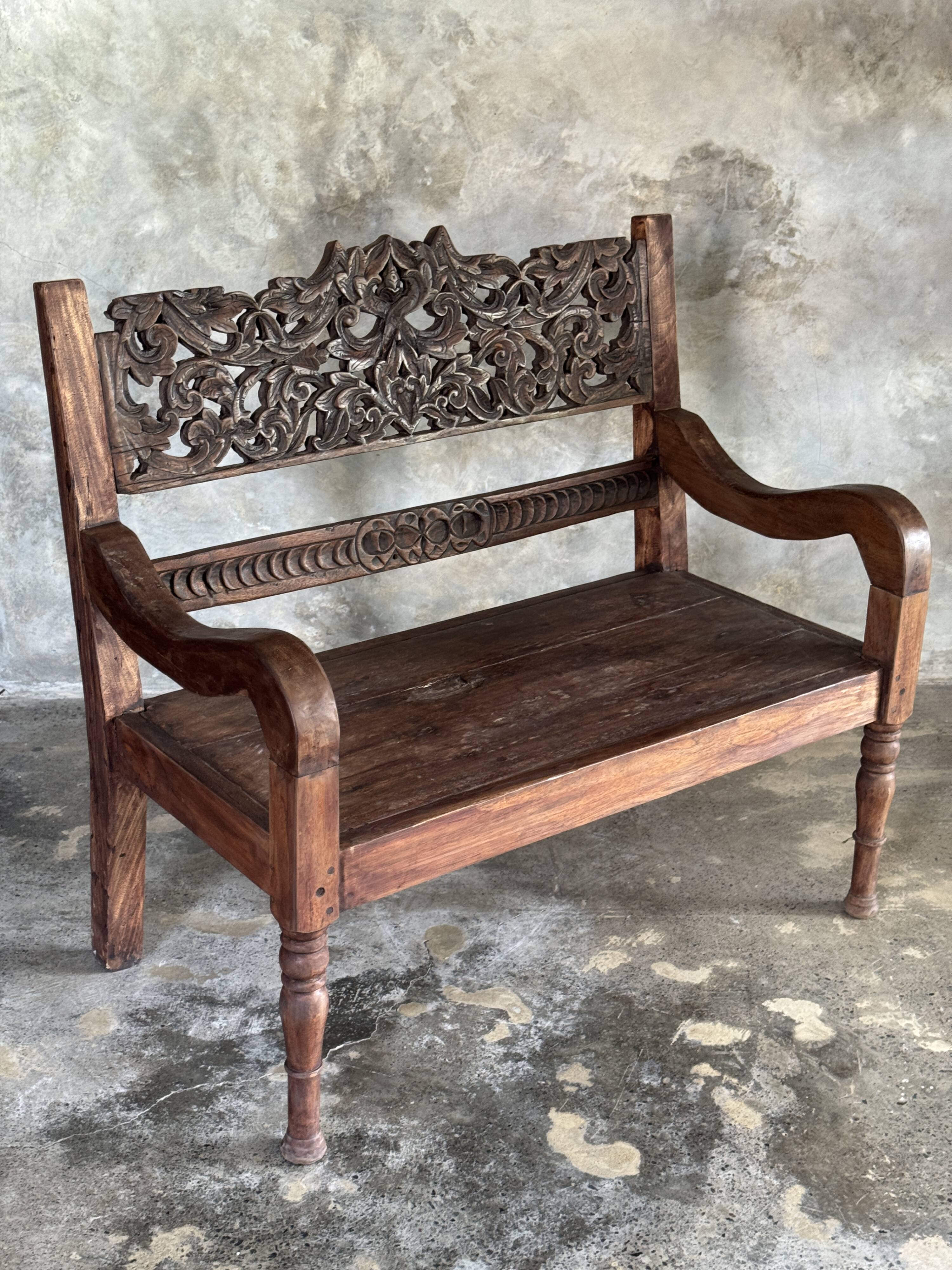 Small antique Indonesian bench in carved teak with plant and floral motifs.