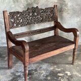 Small antique Indonesian bench in carved teak with plant and floral motifs.