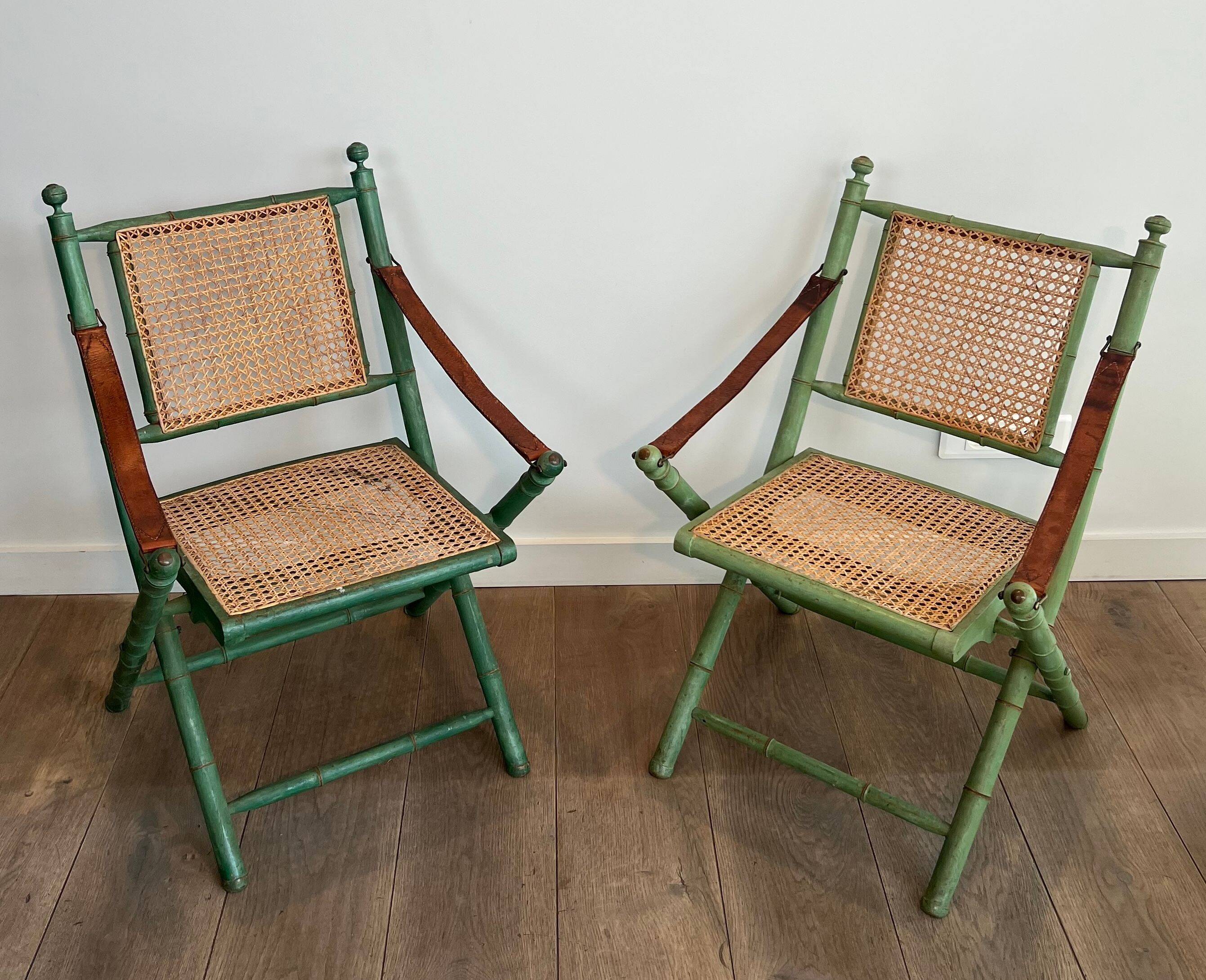 Paire de chaises safari pliantes façon faux-bambou patiné, dossiers et assises cannées et repose-bras en cuir