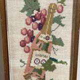 Broderie hollandaise encadrée représentant une vigne avec des raisins, des bouteilles de vin et des paniers