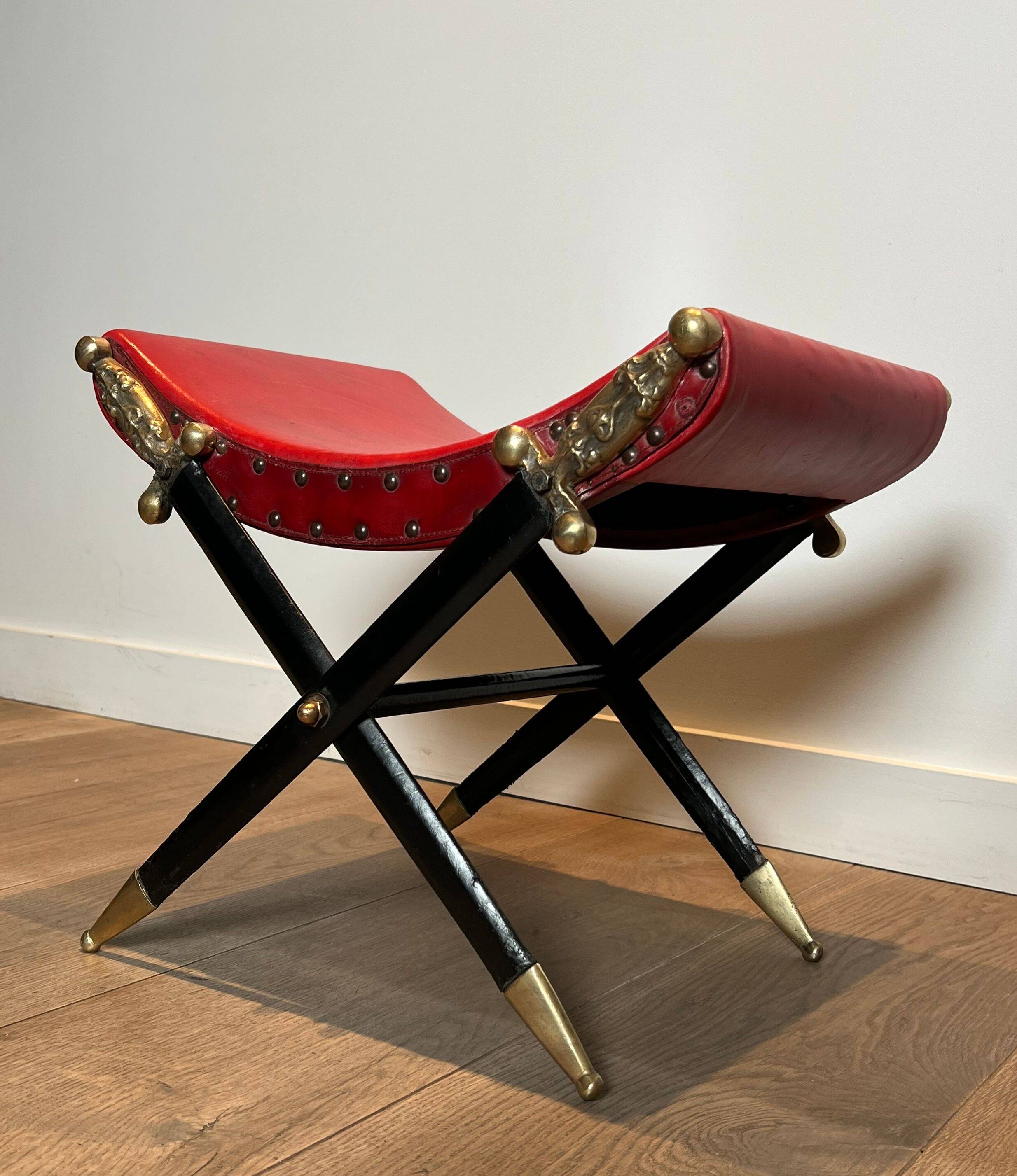 Neoclassical curule stool in red leather, decorated with crossed swords in bronze and metal covered in black leather.