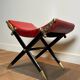 Neoclassical curule stool in red leather, decorated with crossed swords in bronze and metal covered in black leather.