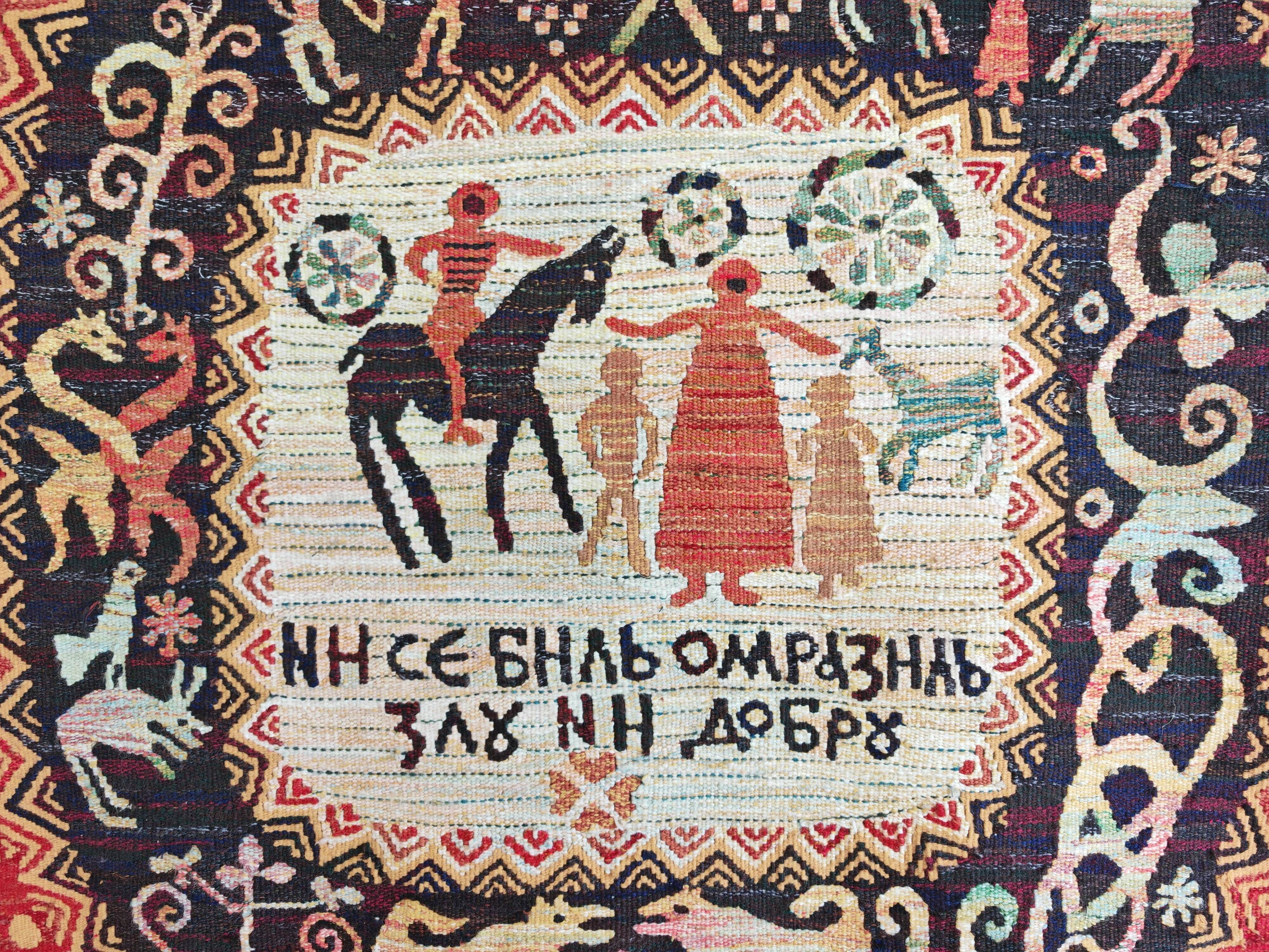 Vintage handwoven tapestry with a folk scene and archaic Slavic writing.