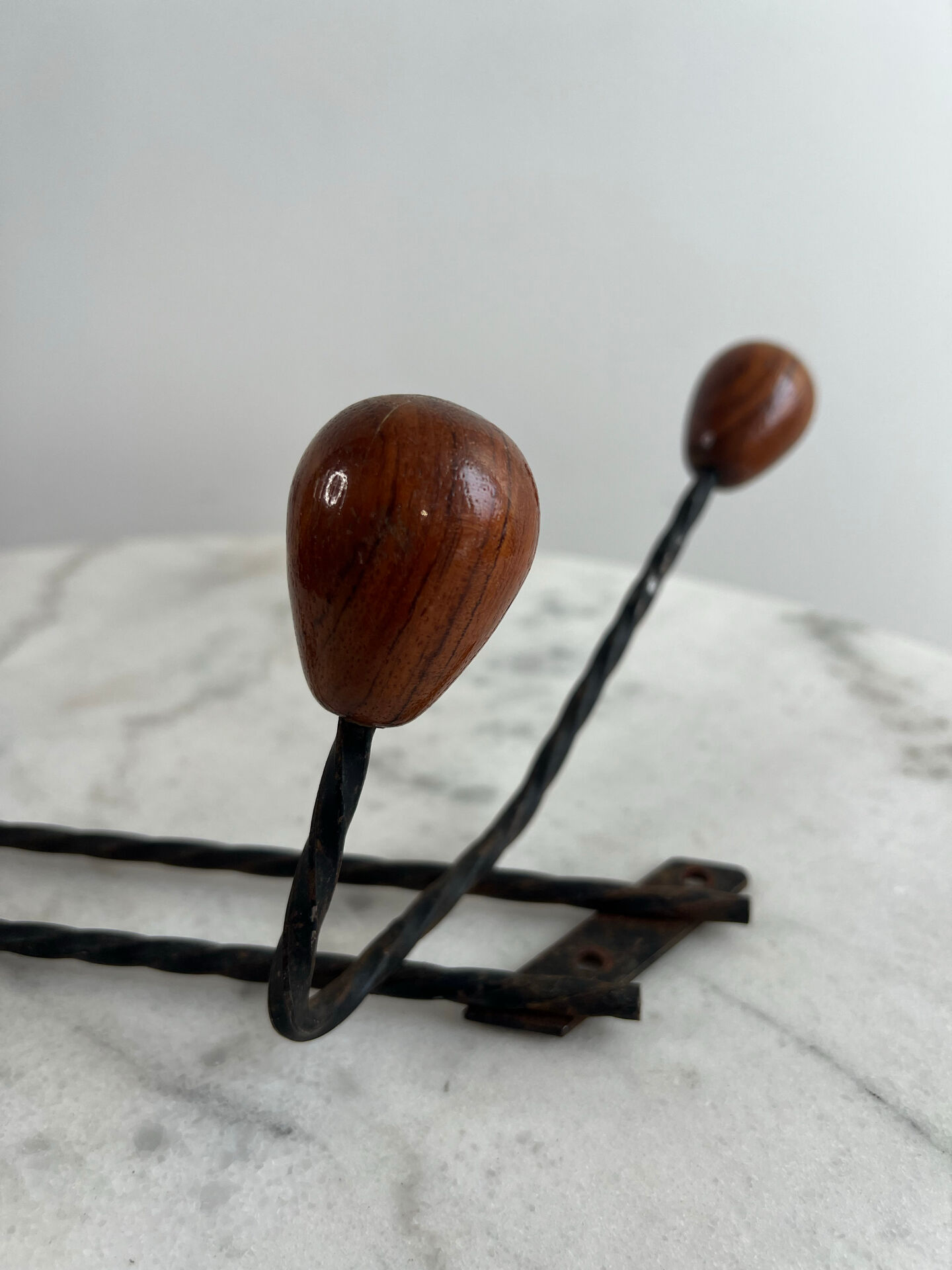 Wall-mounted coat rack in wrought iron with turned wooden knobs.