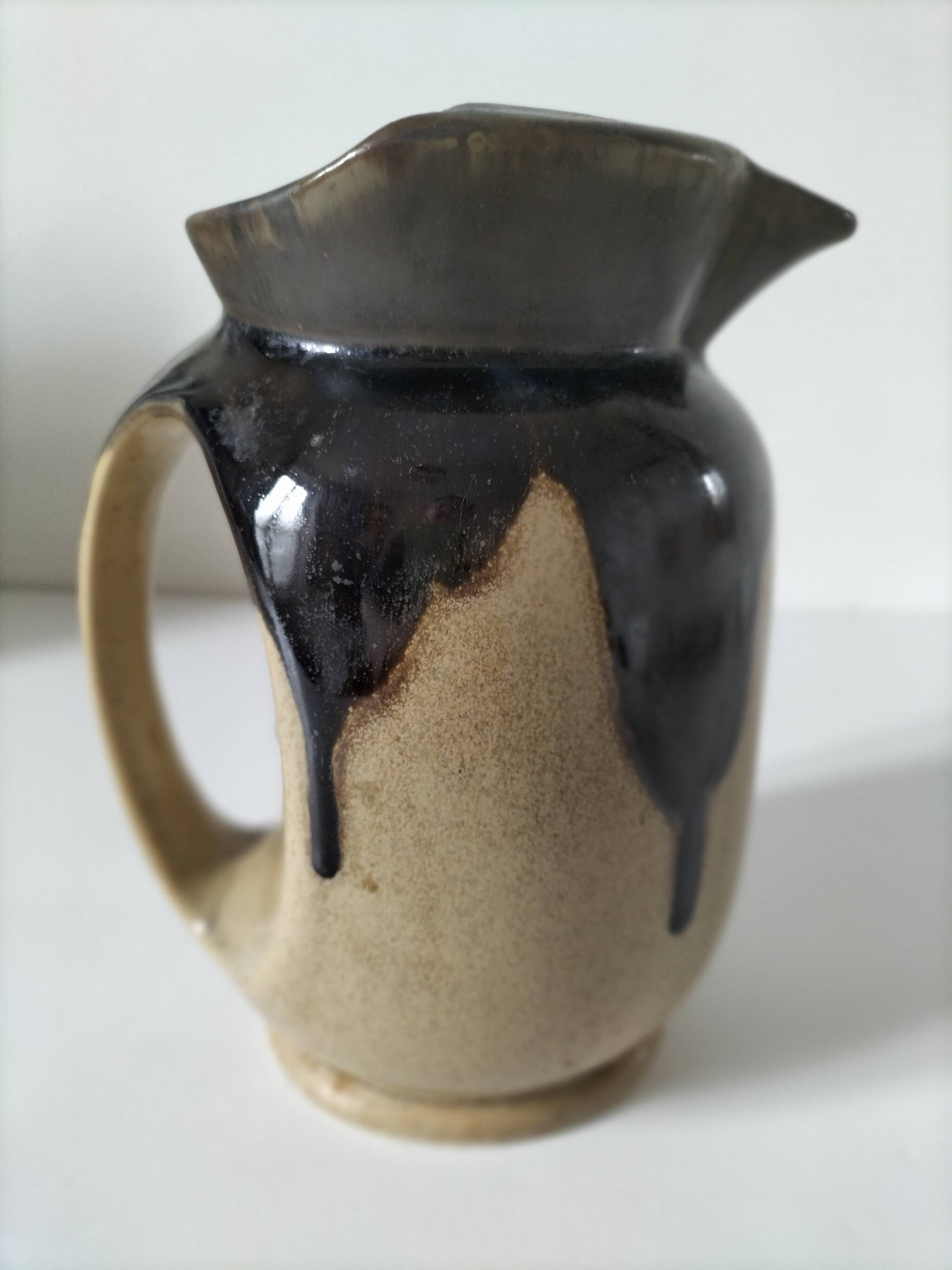 Stoneware jug with deep black drips on a sandy background.