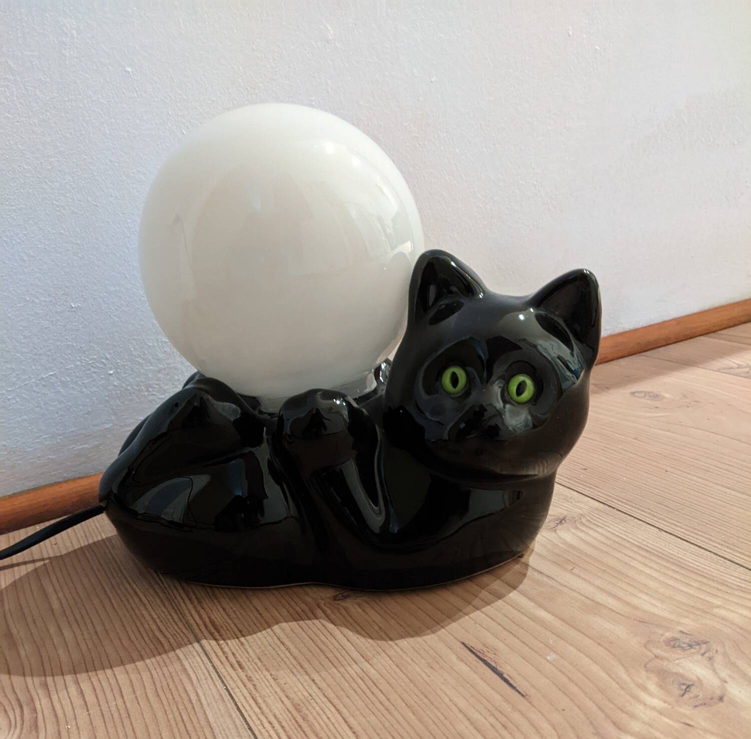 Black cat playing with its globe table lamp