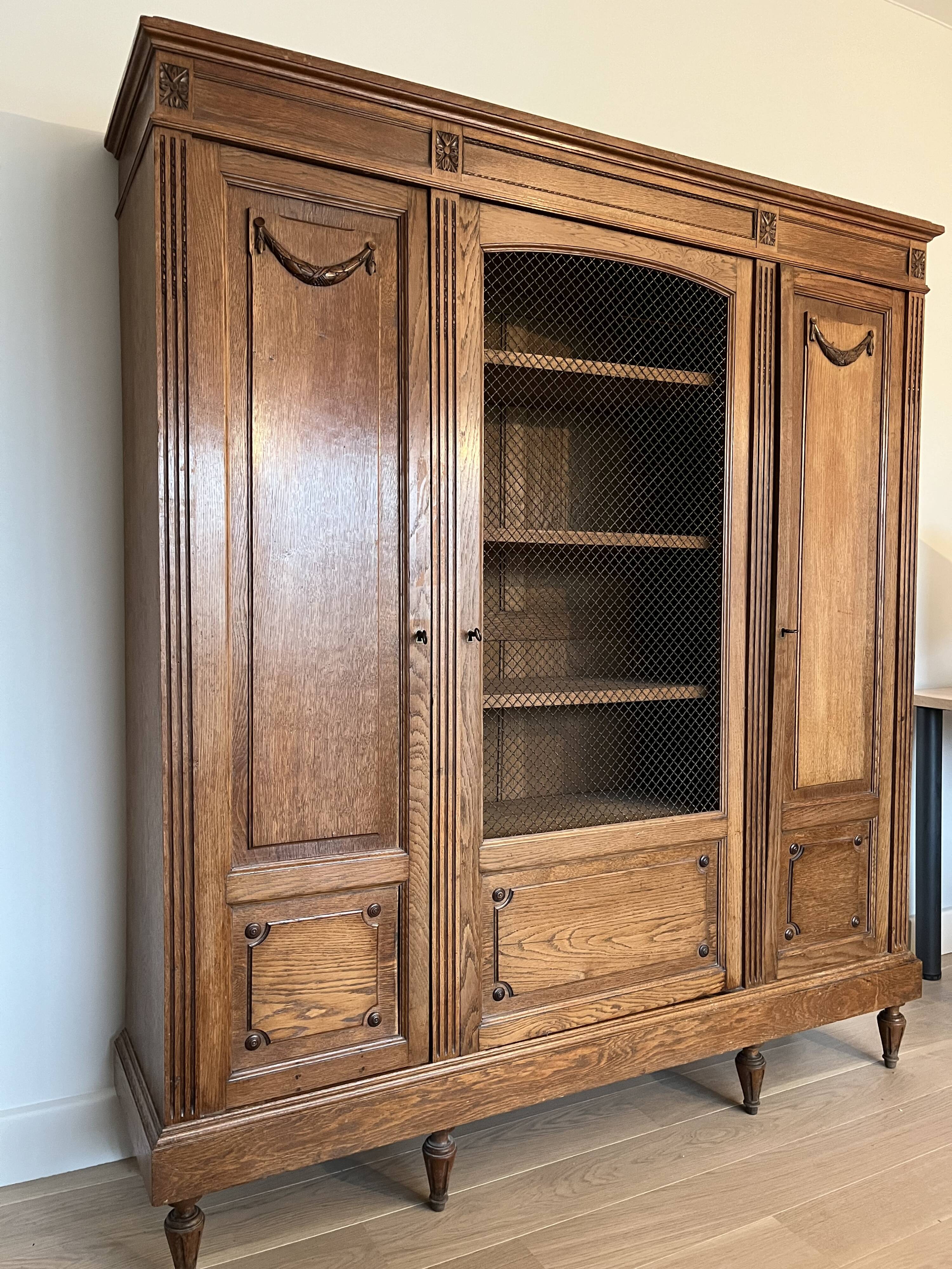 Three-door glass display cabinet with a grille in the Louis XVI style, antique and decorated.