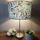 Table lamp with chrome stem, tropical plant shade.