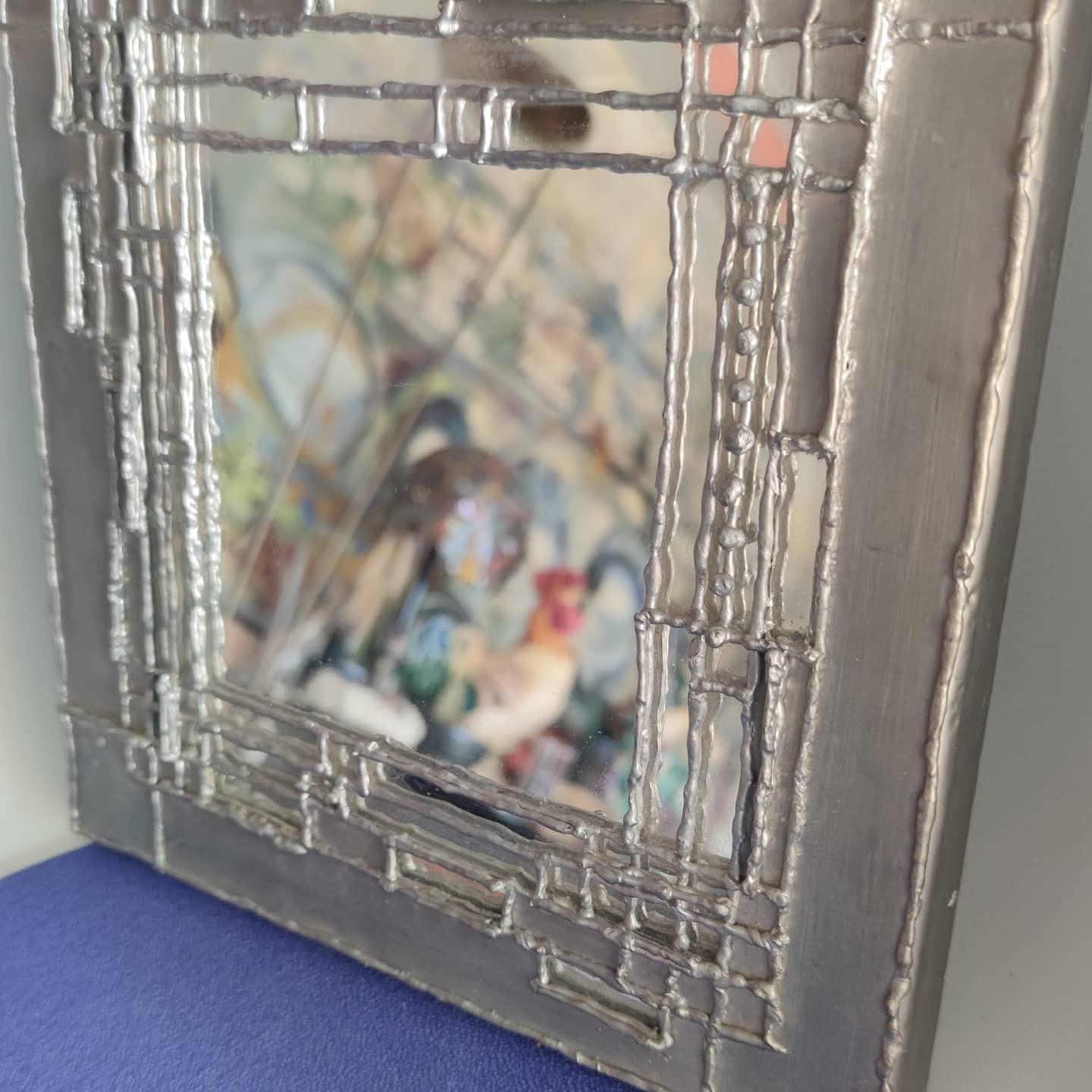 Pewter mirror on a brutalist-style wooden stand