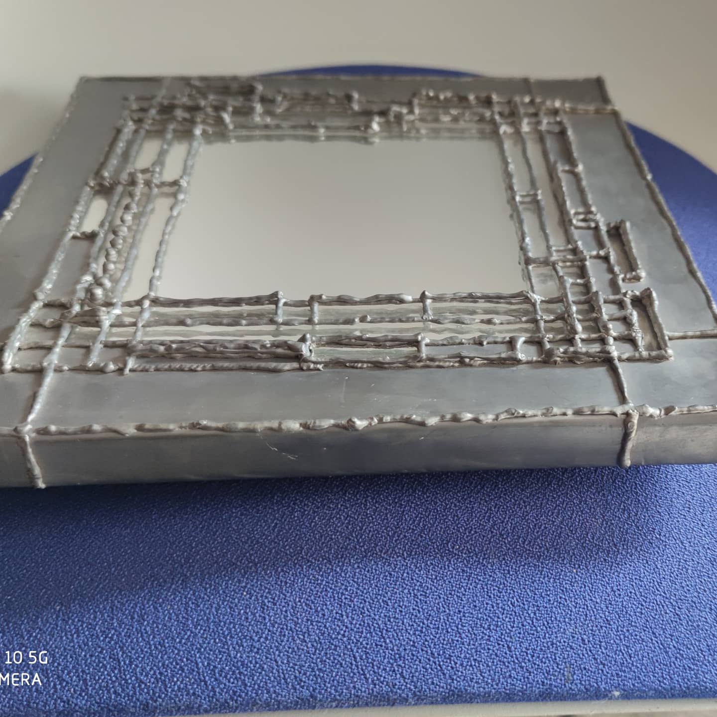 Pewter mirror on a brutalist-style wooden stand