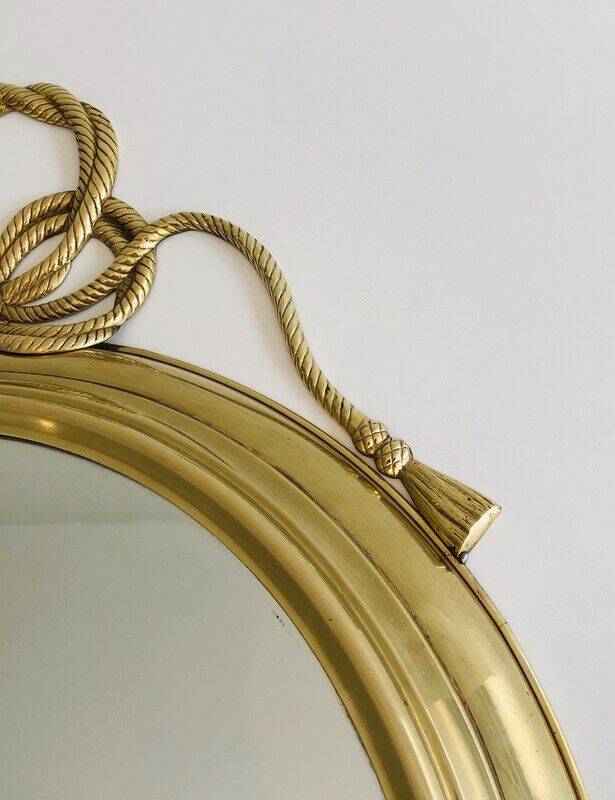 Large decorative oval mirror in brass adorned with a significant twisted bow.