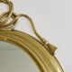 Large decorative oval mirror in brass adorned with a significant twisted bow.