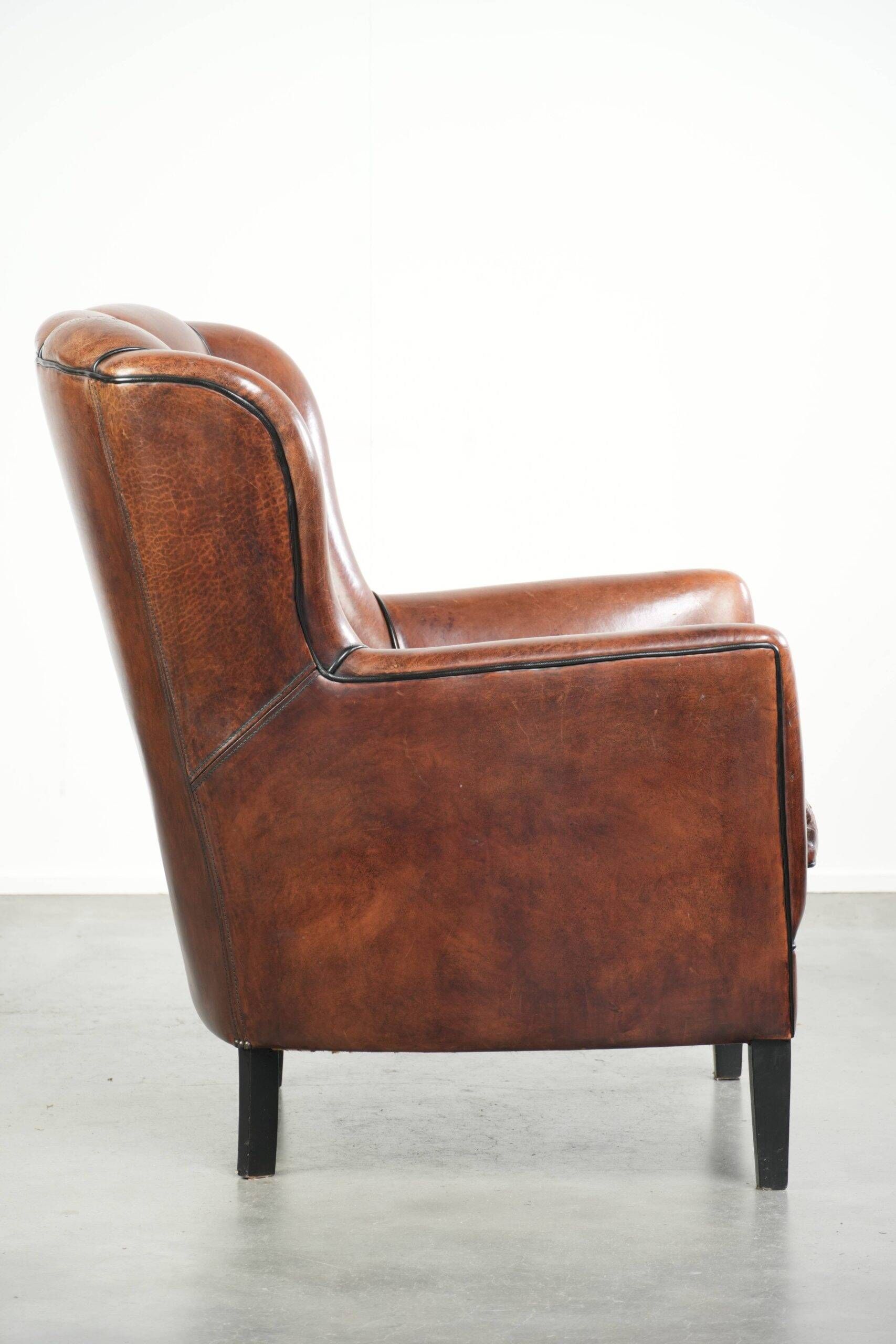 Fauteuil en peau de mouton confortable au design unique, fini avec un passepoil noir.