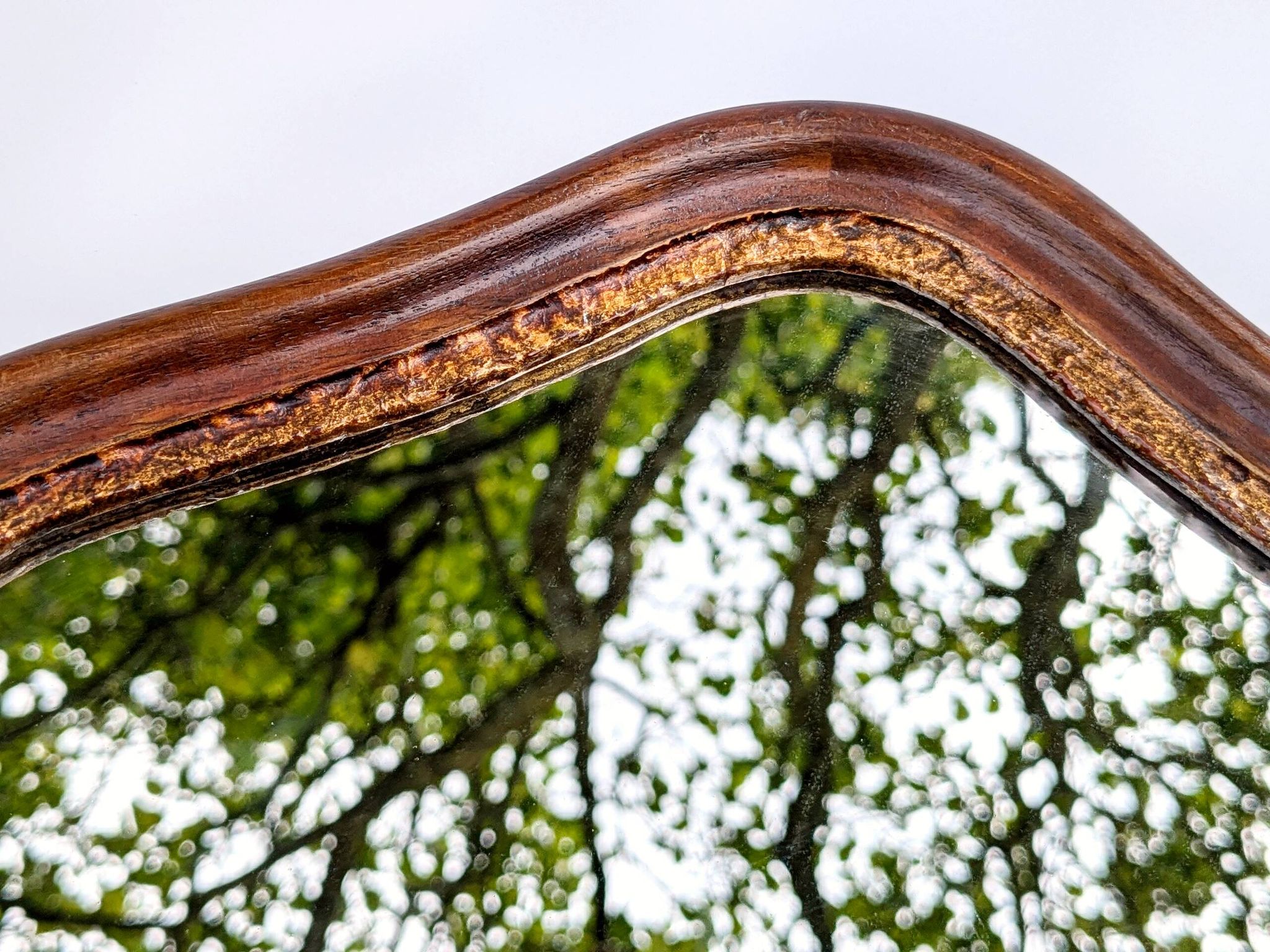 Antique wall mirror in carved wood with a wavy shape and a golden trim.