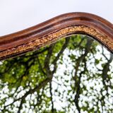 Antique wall mirror in carved wood with a wavy shape and a golden trim.