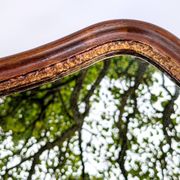 Antique wall mirror in carved wood with a wavy shape and a golden trim.