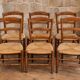 Set of six rustic chairs in natural wood with straw seats.