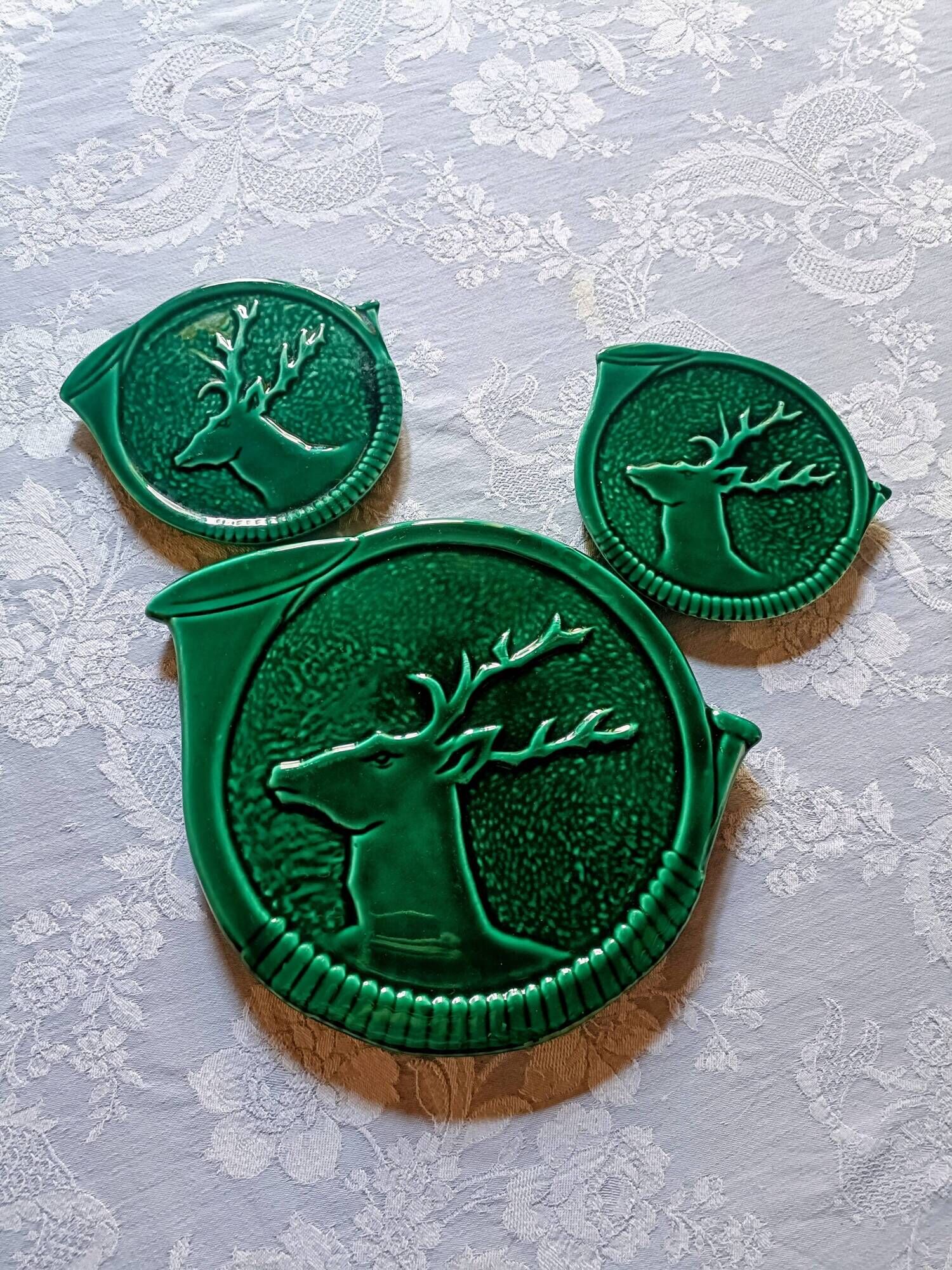 A trivet and two bottle holders in green Vallauris majolica.