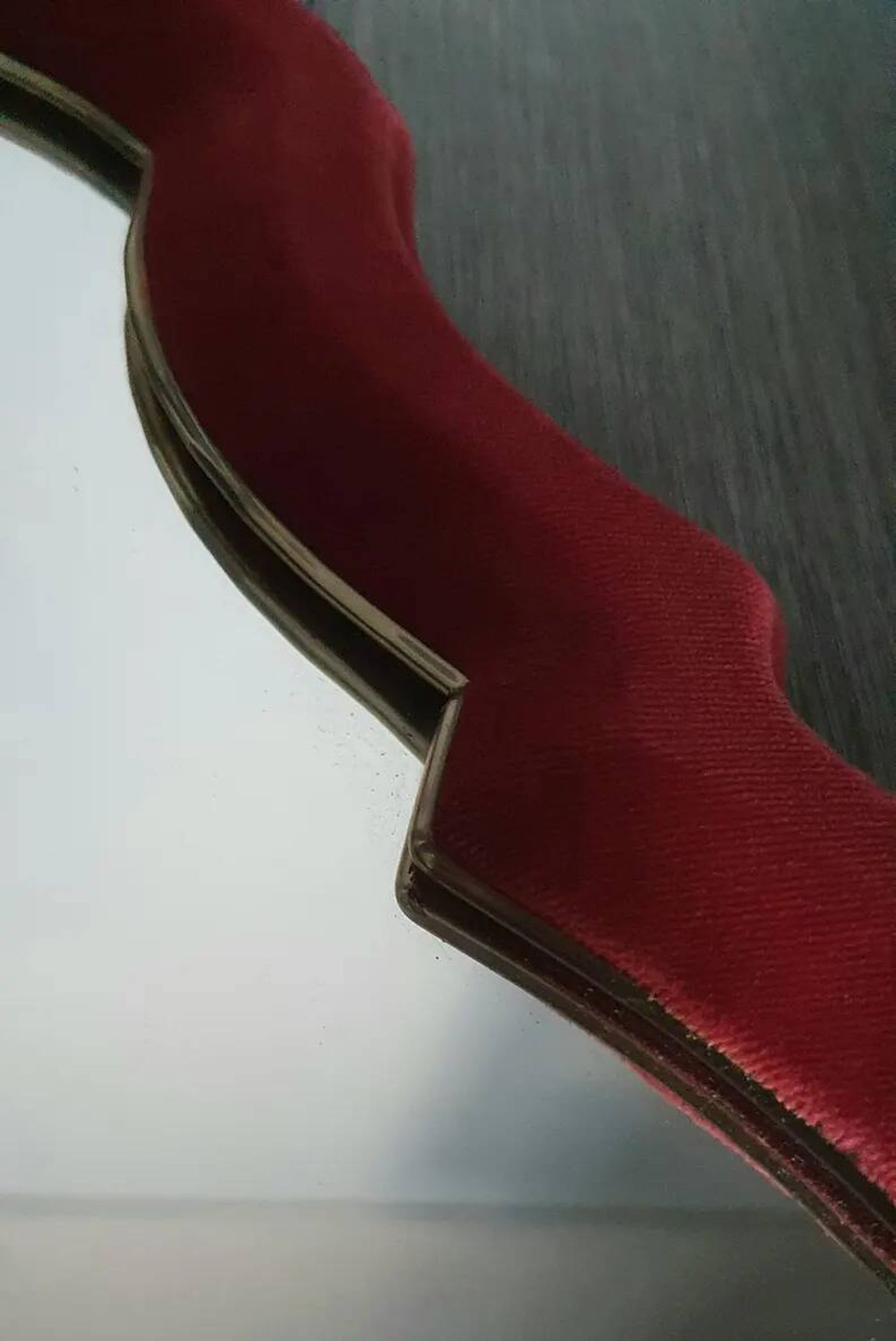 Vintage mirror with a scalloped shape in burgundy velvet and a golden trim.