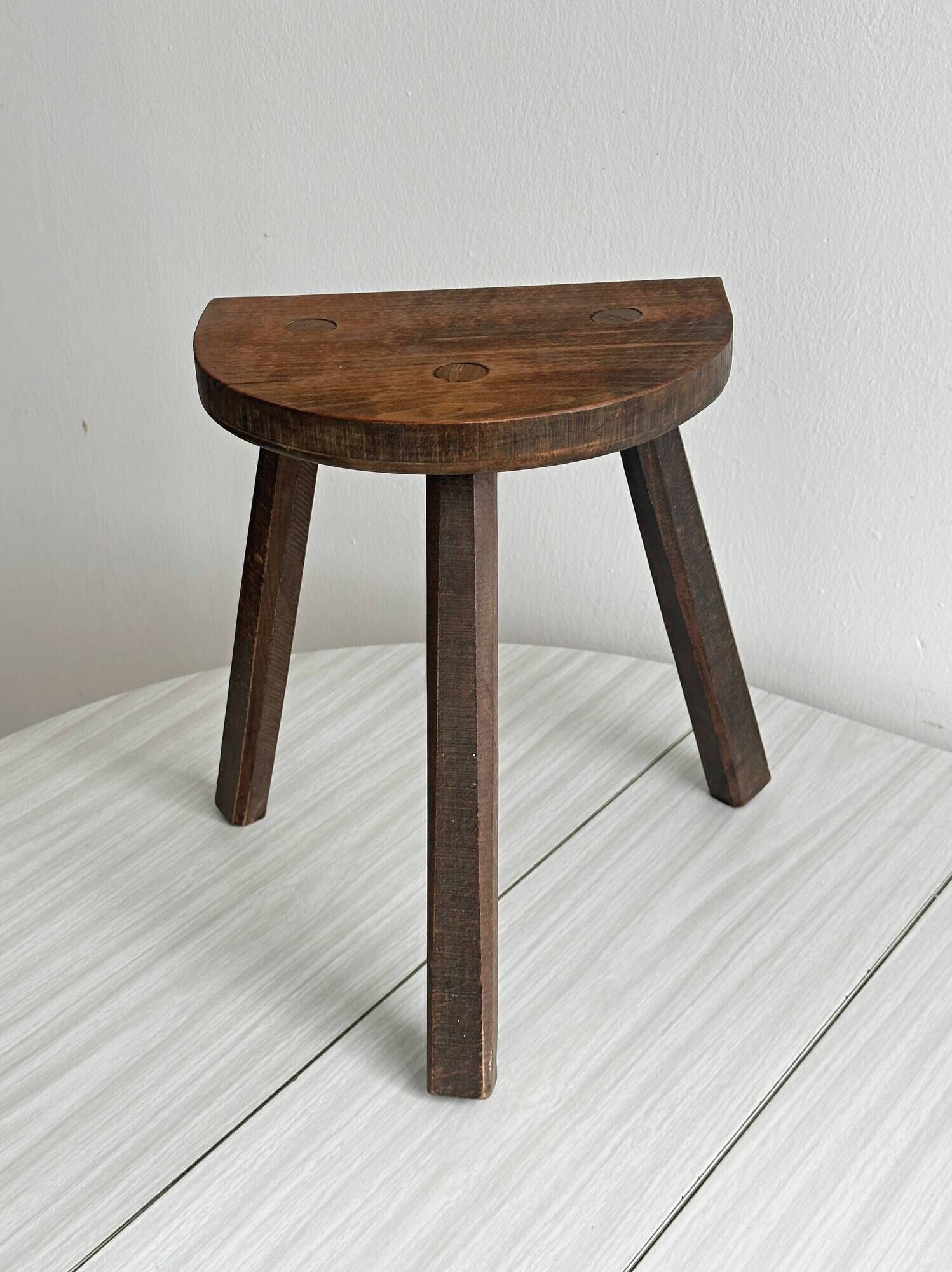 Antique wooden tripod stool with a semi-circular seat.