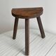 Antique wooden tripod stool with a semi-circular seat.