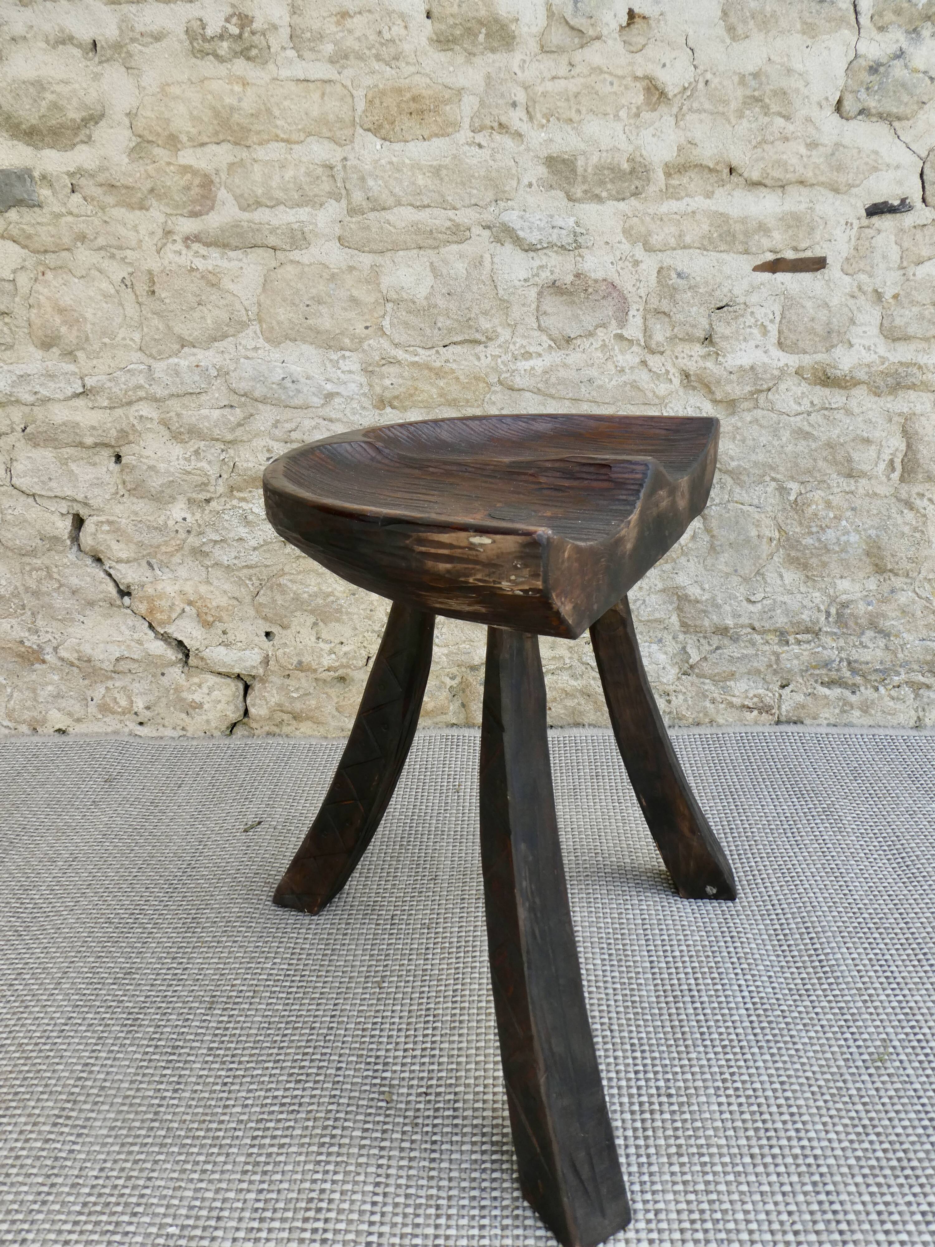 Tripod stool made of solid wood, with a carved seat.