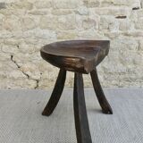 Tripod stool made of solid wood, with a carved seat.