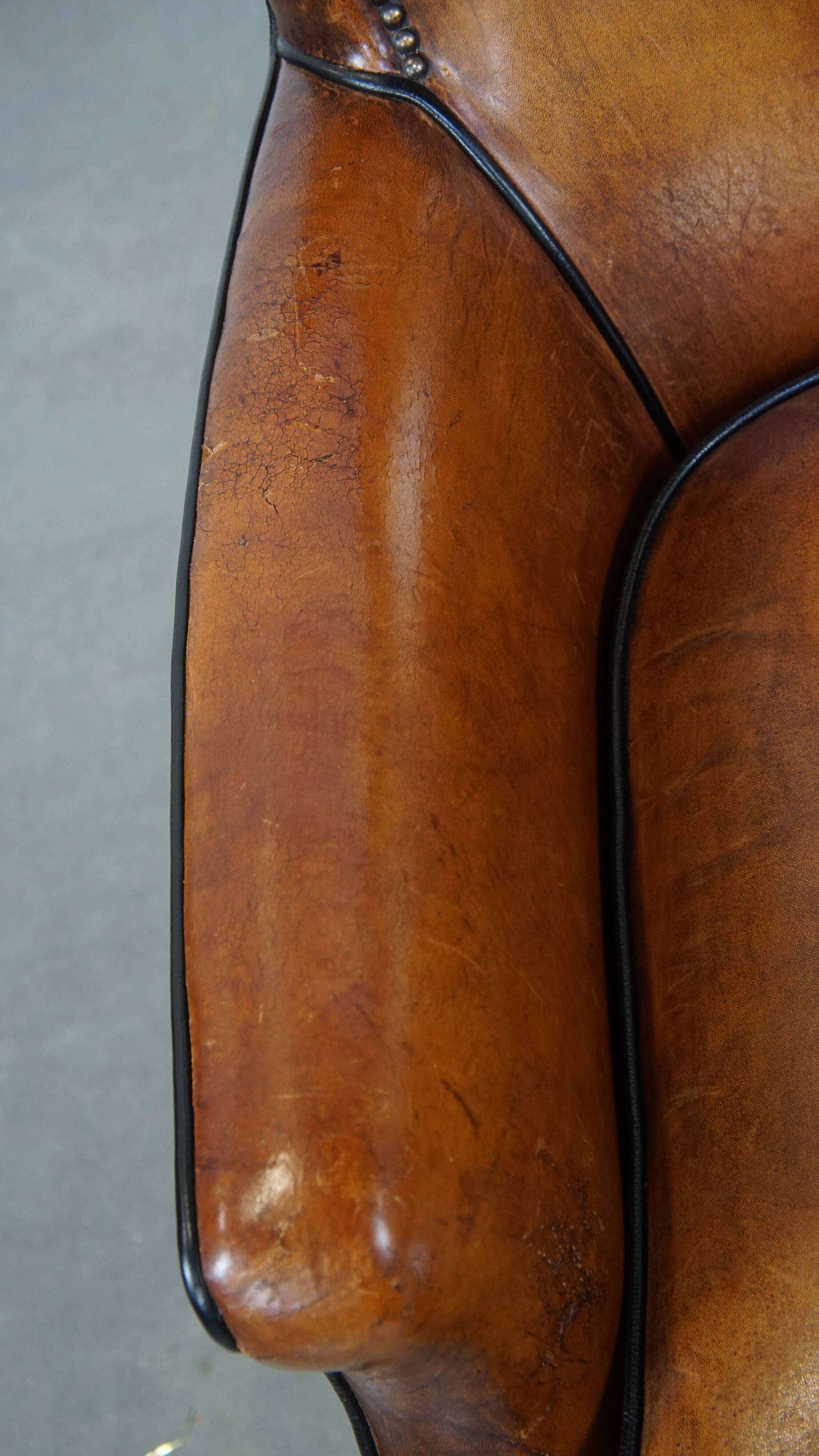 Cognac-colored sheepskin armchair with black piping and decorative nails
